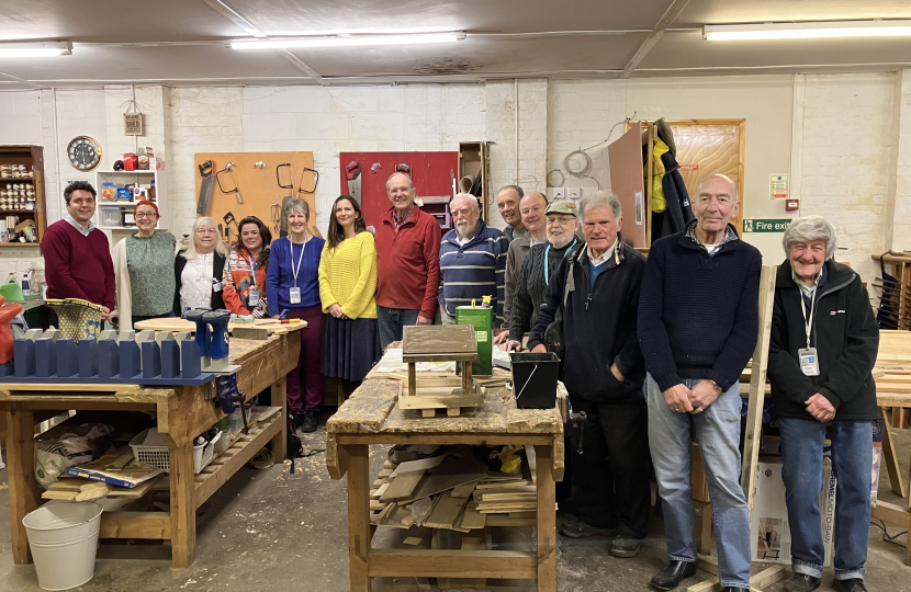 Huw stood with members of Bexhill Men's Shed around workbenches and tools